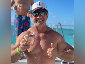 A man enjoys a refreshing cocktail while giving a thumbs up, capturing the fun and festive atmosphere of a day on the water with friends.