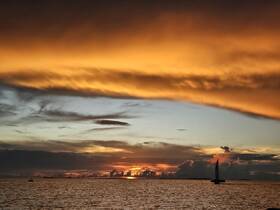 A stunning sunset over the horizon with a sailboat silhouetted against the vibrant sky, perfect for capturing the beauty of evening cruises.