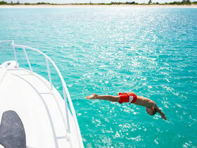 A child joyfully dives into the crystal-clear turquoise waters from the bow of a boat, capturing the essence of summer fun and adventure on the water.