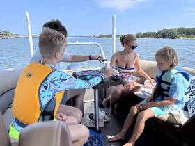 A family enjoys a relaxing day on a boat, with kids in life jackets and adults engaging in conversation — perfect for summer outings on the water.