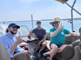 A cheerful group of friends enjoying a day on a pontoon boat, giving thumbs up and celebrating the perfect day on the water.