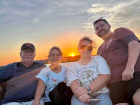 A joyful family poses for a photo against a stunning sunset backdrop, capturing a memorable moment on their boating adventure.