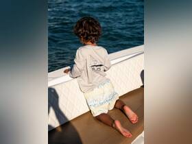 A young child kneels on the deck of a boat, gazing out at the water, capturing the essence of adventure and exploration on the open sea.
