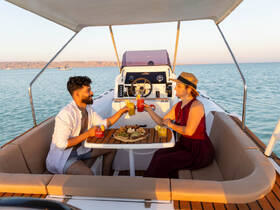 A couple enjoys cocktails and a delicious spread on the deck of a boat, perfect for sunset cruises and romantic getaways on the water.