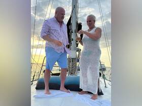 A couple enjoys cocktails on the deck of a sailboat at sunset, capturing a perfect moment of celebration on the water.