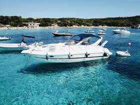 A stunning view of a sleek yacht anchored in crystal-clear waters, surrounded by other boats and a picturesque beach in the background.