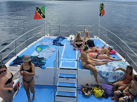 A lively group enjoys sunbathing on the deck of a catamaran, surrounded by calm waters — perfect for a fun day out on the boat.