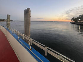 A serene view from a boat's deck at sunset, showcasing the calm waters and a distant pier, perfect for peaceful evening cruises.