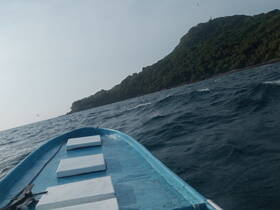 A view from the bow of a small boat navigating through open waters, with a lush green coastline in the background, showcasing the beauty of a maritime adventure.