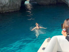 A woman enjoys swimming in the crystal-clear waters of a cave while friends capture the moment from the boat — a perfect snapshot of adventure and fun on the water.
