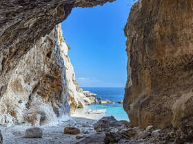 A stunning view from inside a cave, showcasing a small boat anchored near a beautiful beach and clear waters — a perfect destination for exploration and relaxation.