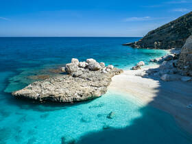 A stunning view of a secluded beach with crystal-clear turquoise waters and rocky formations, perfect for a tranquil getaway or exploration.