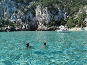 Two snorkelers explore the crystal-clear waters near a scenic beach, with a boat anchored in the background — a perfect setting for aquatic adventures.