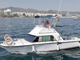 A couple enjoys a scenic ride on their boat, navigating through beautiful waters with a picturesque coastal backdrop.