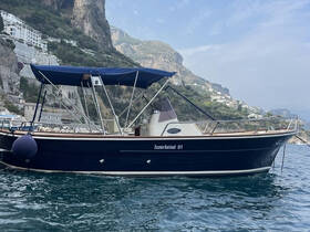 A beautiful side view of a boat anchored near a stunning coastal landscape, showcasing the vessel's elegant design against the backdrop of cliffs and buildings.