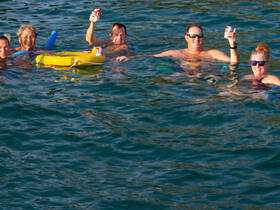 A cheerful group enjoys a refreshing swim while toasting with drinks in the water, capturing the essence of fun and relaxation on a sunny day.