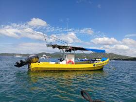 A vibrant yellow speedboat anchored in calm waters, showcasing its sleek design against a picturesque backdrop of hills and clouds.