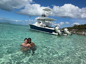 A couple enjoys a refreshing swim in crystal-clear waters with a boat anchored nearby, perfect for a romantic day on the water.