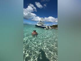 A couple enjoys a refreshing swim in crystal-clear turquoise waters with their boat anchored nearby, capturing the essence of a perfect day on the water.