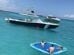 A group of friends enjoys a sunny day on the water, relaxing on a floating mat while a boat is anchored nearby — perfect for summer fun and aquatic adventures.