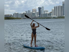 A woman enjoys paddleboarding against a stunning city skyline, showcasing the perfect blend of outdoor adventure and urban scenery.