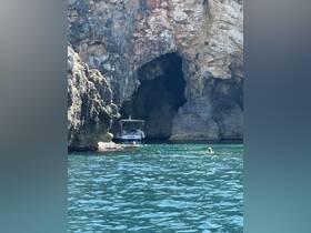 A scenic view of a boat anchored near a rocky cave, with swimmers enjoying the clear waters — a perfect spot for exploration and adventure.