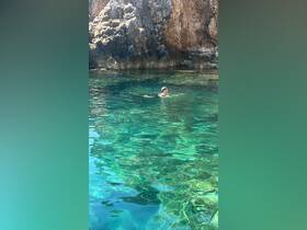 A swimmer enjoys the crystal-clear waters near a rocky coastline, perfect for a refreshing dip during a boating adventure.