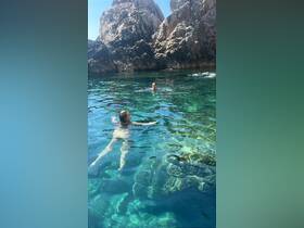 Two swimmers enjoy the crystal-clear waters near a rocky coastline, perfect for a refreshing escape and adventure on the water.