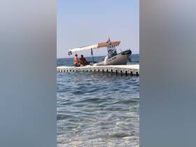 Two men relax on a dock next to a boat taxi, enjoying the serene sea view — a perfect scene for beachgoers looking for transportation.