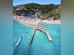 A stunning aerial view of a vibrant beach scene with a bustling pier and turquoise waters, perfect for swimming and relaxation.
