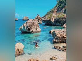 A serene scene of a woman enjoying the crystal-clear waters near rocky formations, perfect for a tropical getaway or beach adventure.