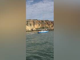 A scenic view of a sailboat with guests enjoying kayaking nearby along a beautiful coastline, perfect for outdoor adventures and family fun on the water.