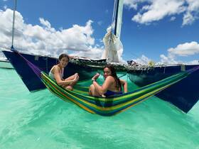 Two girls relax in a colorful hammock suspended from a sailboat, enjoying the turquoise waters and sunny skies — a perfect moment of fun and relaxation on the water.