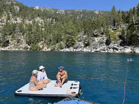 A group enjoys a sunny day on a floating mat in a serene lake, perfect for summer relaxation and fun in the water.