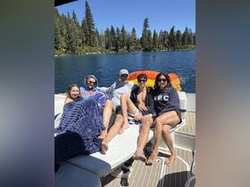 A lively group enjoys a sunny day on the boat, relaxing and sunbathing by the serene waters surrounded by trees — perfect for summer outings and fun with friends.