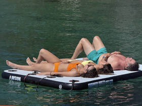 A group of friends relaxes on a floating mat in clear waters, enjoying the sun and each other's company — a perfect day for fun and relaxation on the water.