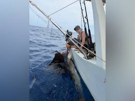 A woman proudly poses with her catch while fishing on a boat in the open ocean — a thrilling moment for any angler.