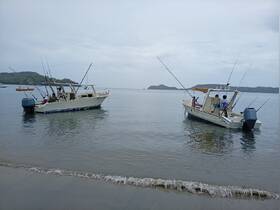 Two fishing boats are anchored in calm waters, with people onboard preparing for a day of fishing. This scene captures the excitement of a fishing adventure in a beautiful coastal setting.
