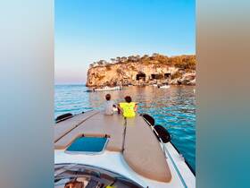 Two children enjoy the serene view from the bow of a boat, overlooking a stunning coastline and rocky cliffs — a perfect moment for family adventures on the water.