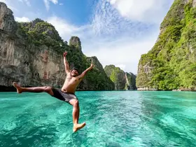 A joyful moment captured as a man leaps into the crystal-clear waters surrounded by stunning cliffs — a perfect representation of adventure and fun in nature.