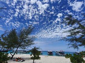 A picturesque beach scene featuring several boats anchored in turquoise waters, with guests enjoying the sunny day — a perfect destination for island adventures.