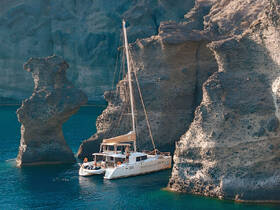 A stunning catamaran anchored near dramatic rock formations, showcasing the beauty of the coastline — perfect for island-hopping adventures.