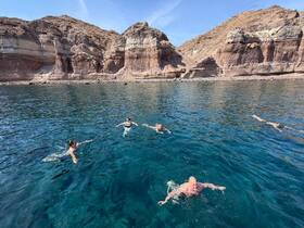 A group of friends enjoys a refreshing swim in crystal-clear waters, surrounded by stunning rocky cliffs — a perfect day for adventure and relaxation.