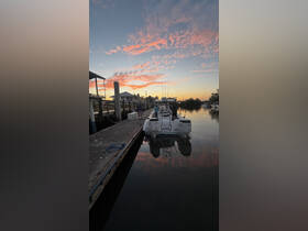 Two individuals prepare for a fishing trip at sunset, with a beautiful reflection of the boat on the calm water — a perfect start to an evening adventure.