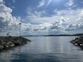 A scenic view of a rocky shoreline with an anchor and a lamp post, set against a backdrop of clouds and water, creating a tranquil atmosphere.
