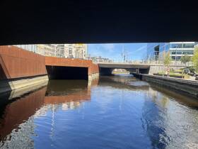 A view of a canal under a bridge, showcasing urban architecture and reflections in the water.