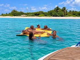 A lively group enjoys a sunny day on a floating mat in crystal-clear waters, perfect for relaxation and fun under the sun.