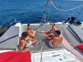 A group of friends relaxes on the netting of a catamaran, enjoying drinks and the sun — an ideal setting for a day on the water.