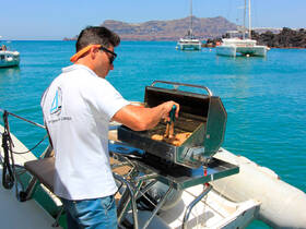 A crew member grills delicious food on a boat, showcasing onboard catering amenities against a stunning turquoise backdrop — perfect for a memorable dining experience at sea.