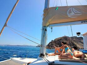 A group of friends enjoys a sunny day sailing on a catamaran, taking in the stunning coastal views — perfect for summer adventures on the water.